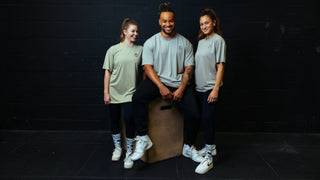 Zwei Frauen und ein Mann sitzen auf einer Plyobox und tragen Unisex T-Shirts von Lifters Wear